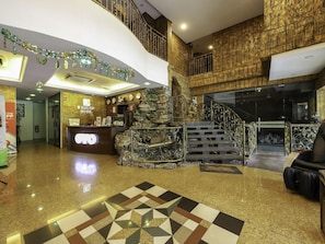 A hotel lobby with a reception desk, a staircase, and a decorative wall.