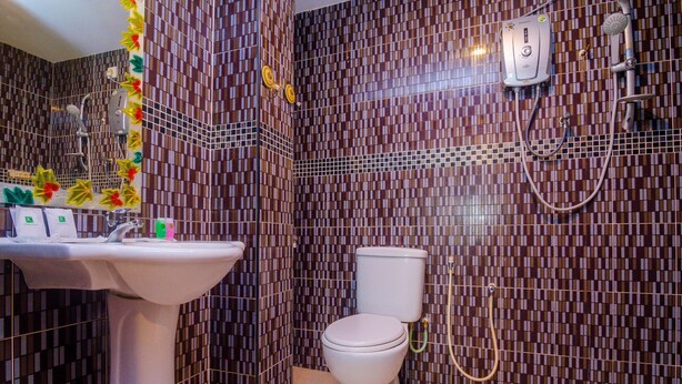 A bathroom with a white sink, toilet, and shower. The walls are tiled with a patterned design. - OYO 562 K Garden Hotel (Sungai Petani)