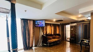 Un hall espacioso con suelo de mármol, un sofá, un televisor montado en la pared y un pilar decorativo.