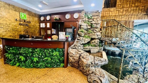 Un área de recepción con un mostrador de madera, una pared verde con diseño de hojas y una pared de piedra con fuente de agua.