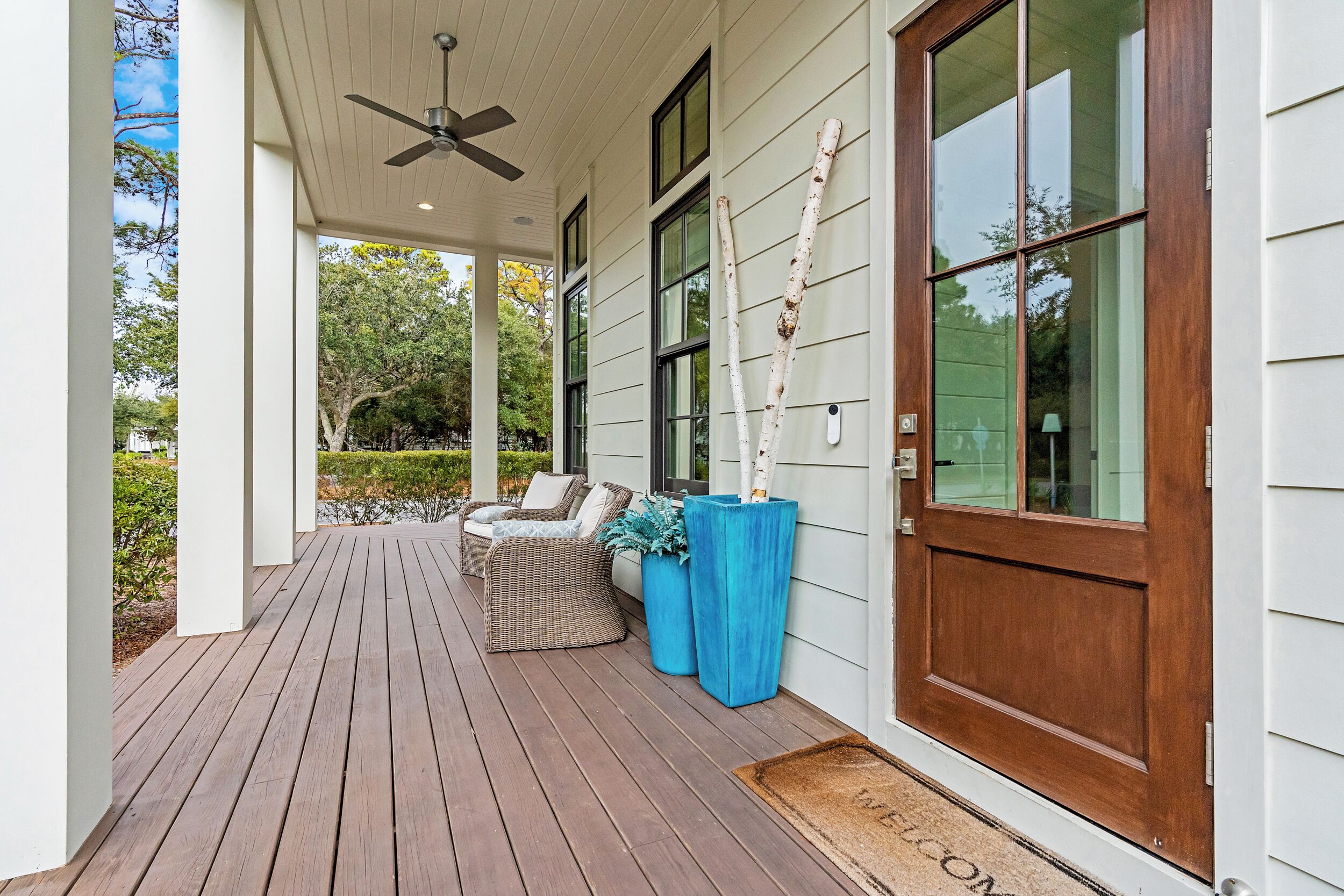 A covered porch with a ceiling fan, a wooden door, and a bench with cushions.