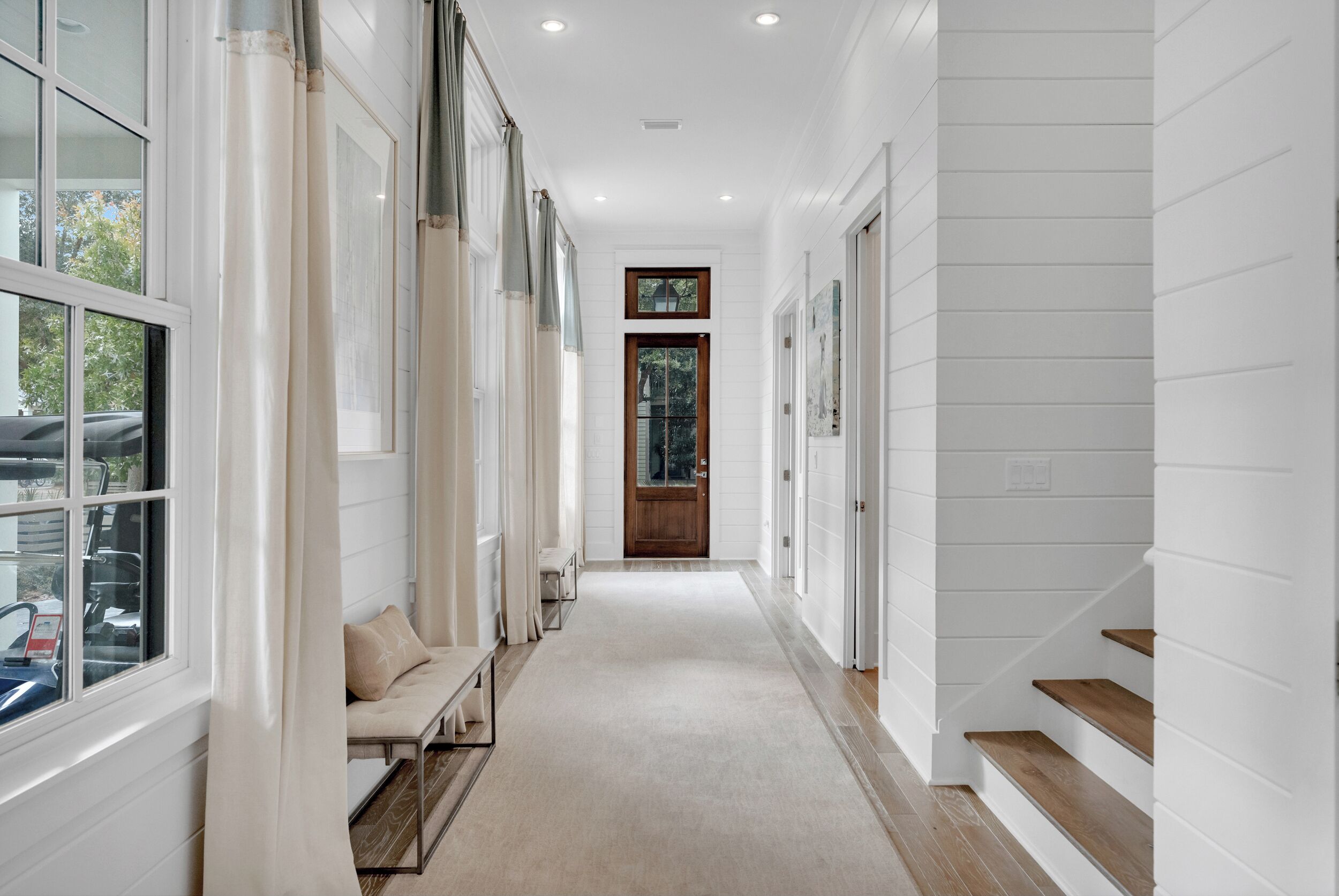 A hallway with a bench, a wooden door, and a staircase.
