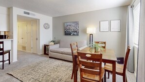 A living room with a sofa, a dining table with chairs, a lamp, and a clock on the wall.