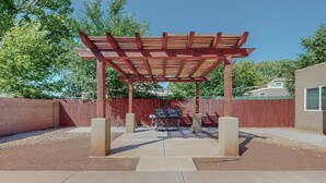 A covered patio area with a pergola, outdoor grill, and concrete seating.