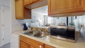 A modern kitchen with wooden cabinets, a stainless steel sink, a coffee maker, a microwave, and a dish drying rack.