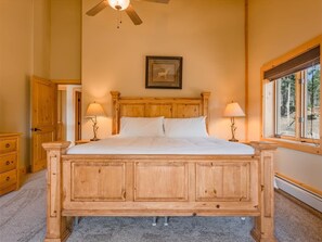 Ein hölzernes Himmelbett mit zwei Nachttischlampen, einem Deckenventilator und einem gerahmten Bild an der Wand.