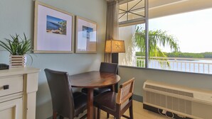 A dining area with a table and chairs, a lamp, a radiator, and framed pictures on the wall.