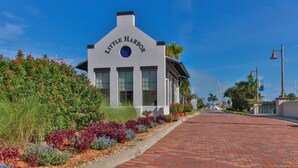 A building named Little Harbor with a clear sky, a brick pathway, and a variety of colorful plants in the foreground.