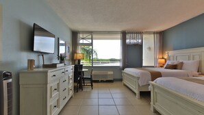 A hotel room with two beds, a desk, a chair, a TV, and a window with a view.