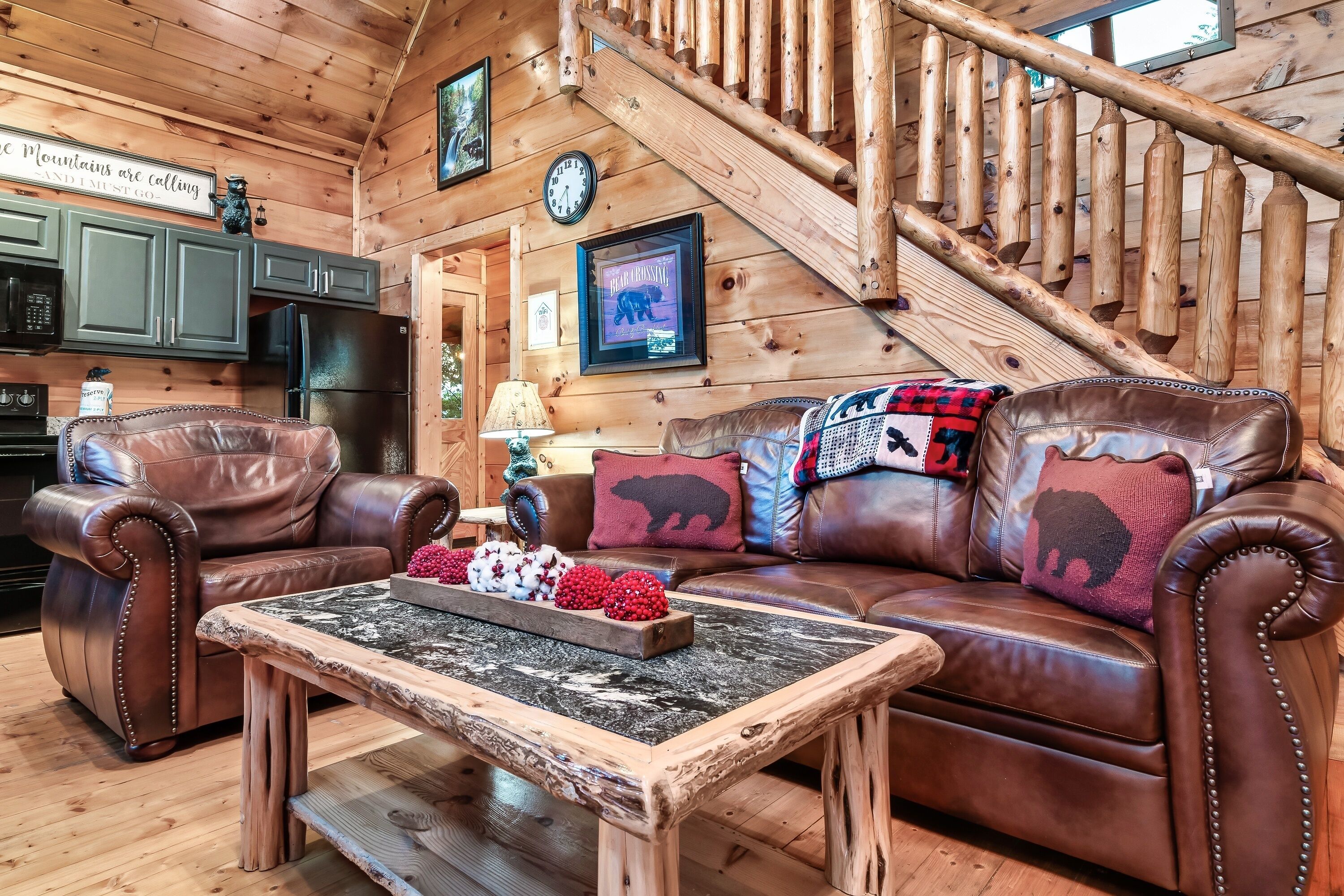 Un intérieur de chalet chaleureux avec un escalier en bois, des meubles en cuir et un coin cuisine.