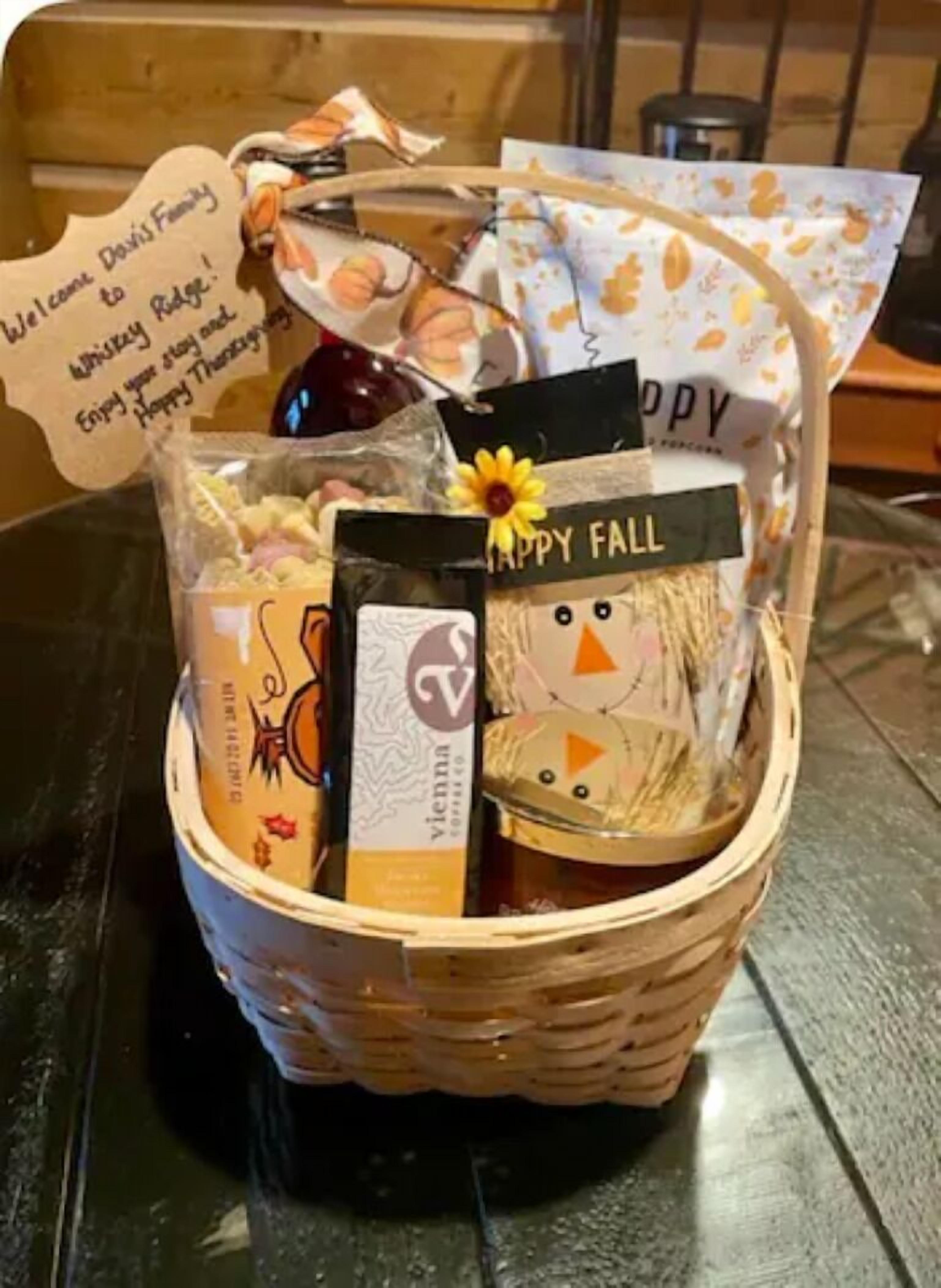 Un panier en osier rempli de divers objets, notamment une bouteille, un paquet de café et une pancarte sur laquelle on peut lire « Joyeuses fêtes d’automne ».