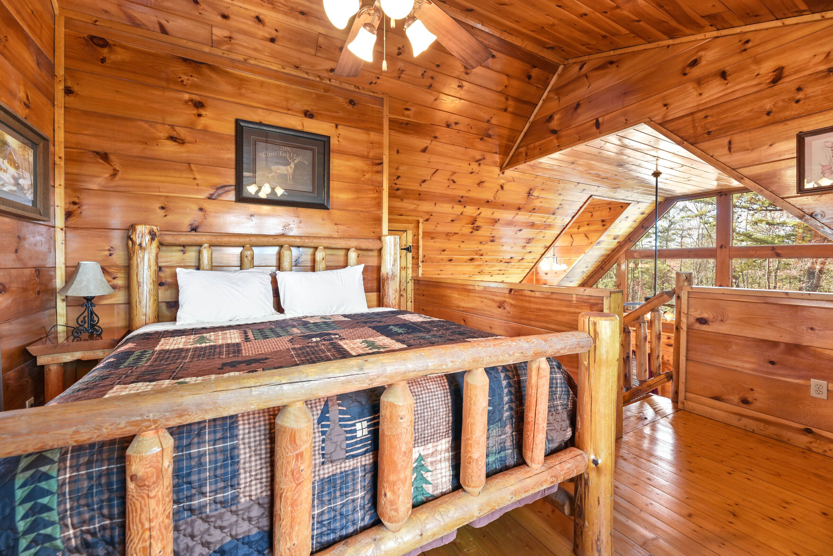 Un dormitorio de cabaña de madera con una cama grande, cabecera de madera y un ventilador de techo.