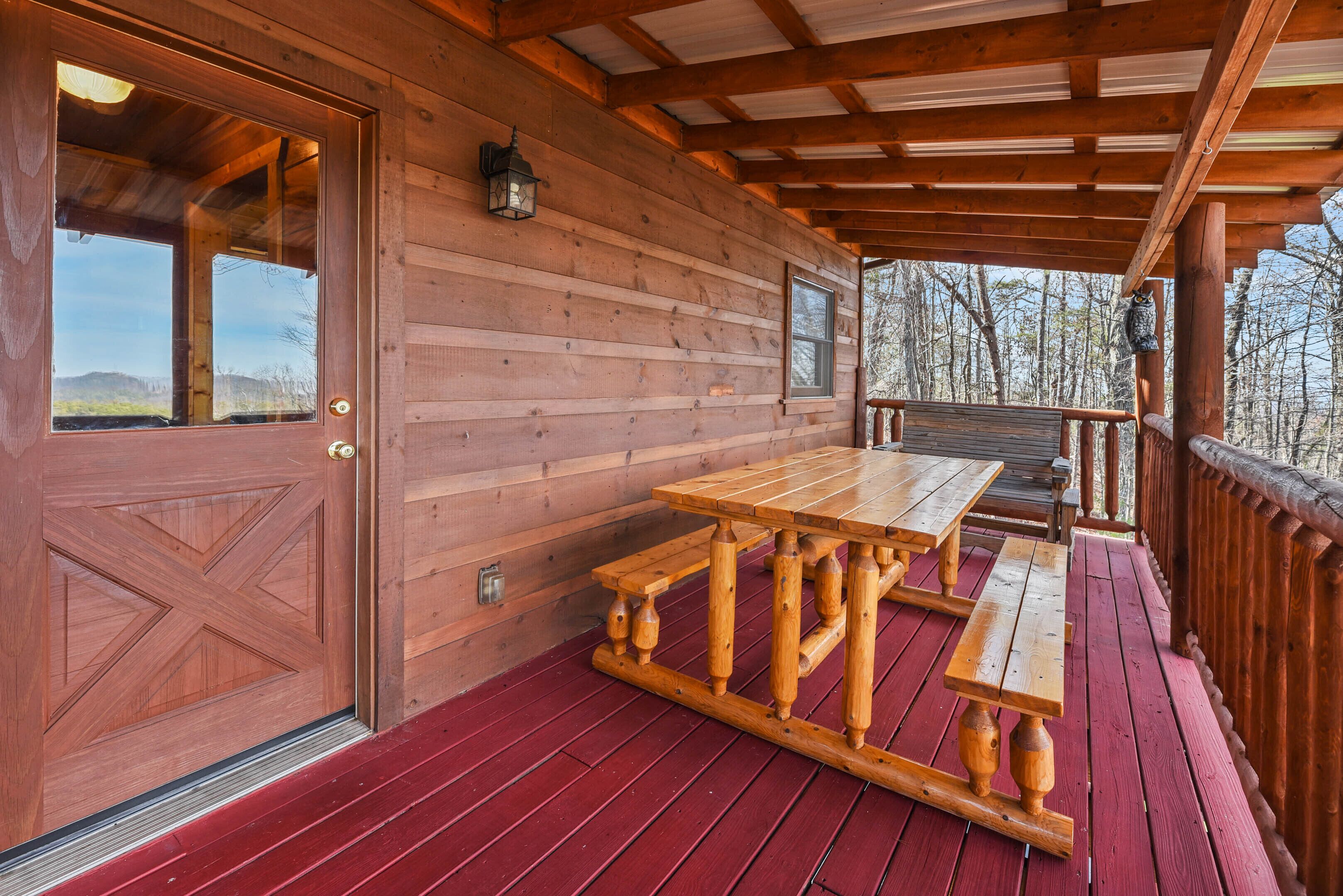 A wooden cabin with a red deck, a large wooden table, and a bench.