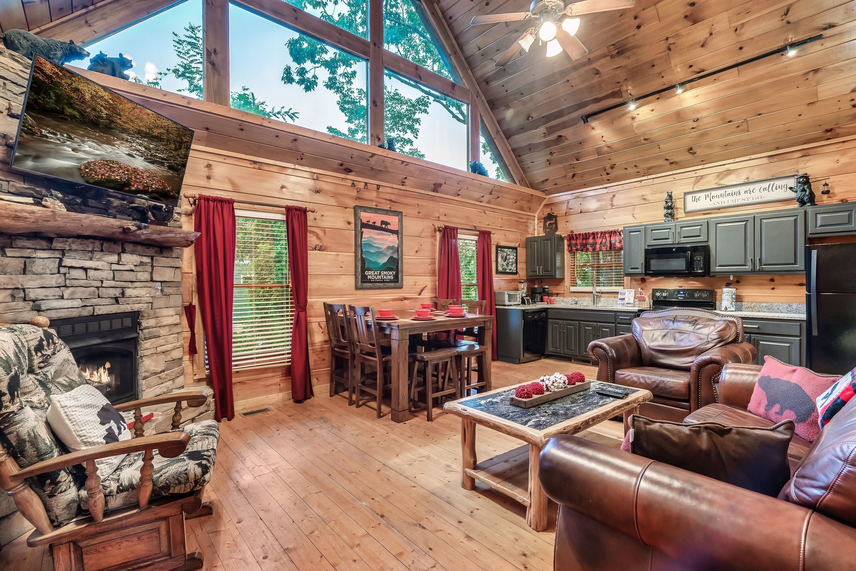 Een gezellig cabin interieur met een stenen open haard, een houten eettafel, leren banken en een keukenhoek.