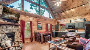 Een gezellig cabin interieur met een stenen open haard, een houten eettafel, leren banken en een keukenhoek.