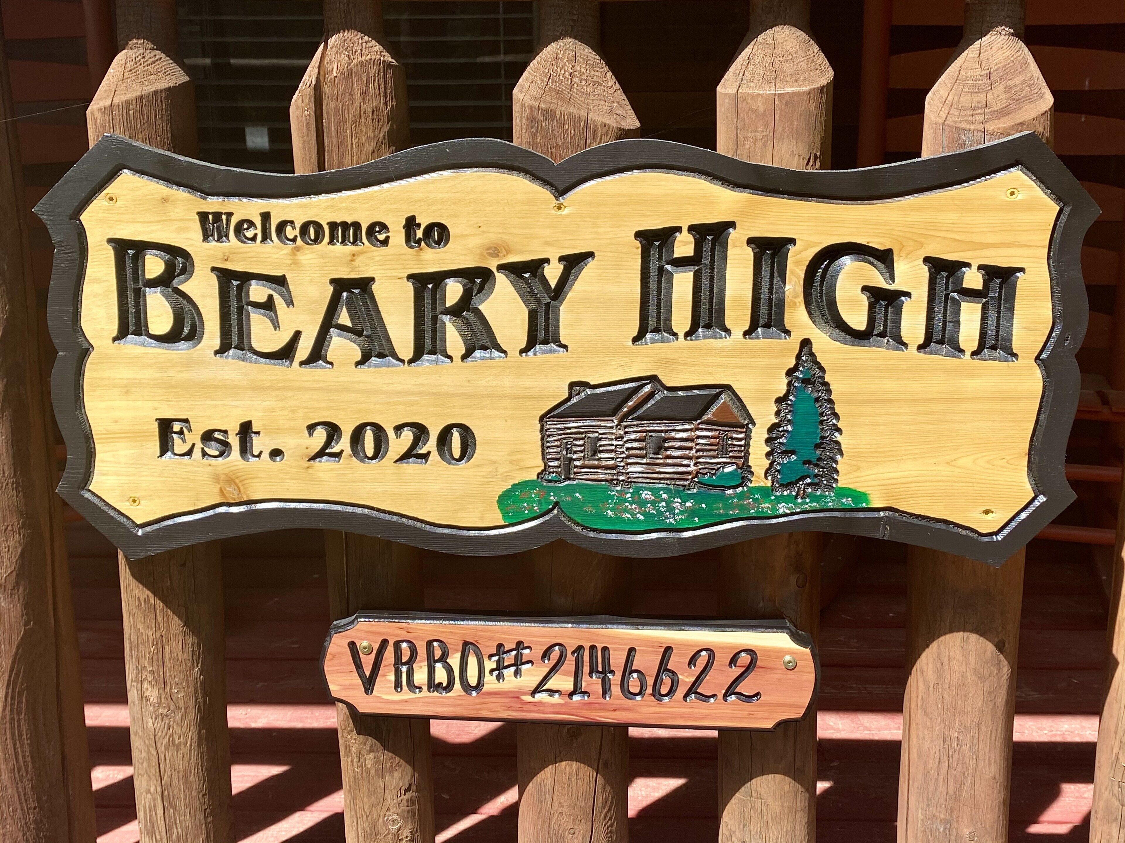 Un letrero de madera da la bienvenida a Beary High, con una ilustración de una cabaña y un número de registro.