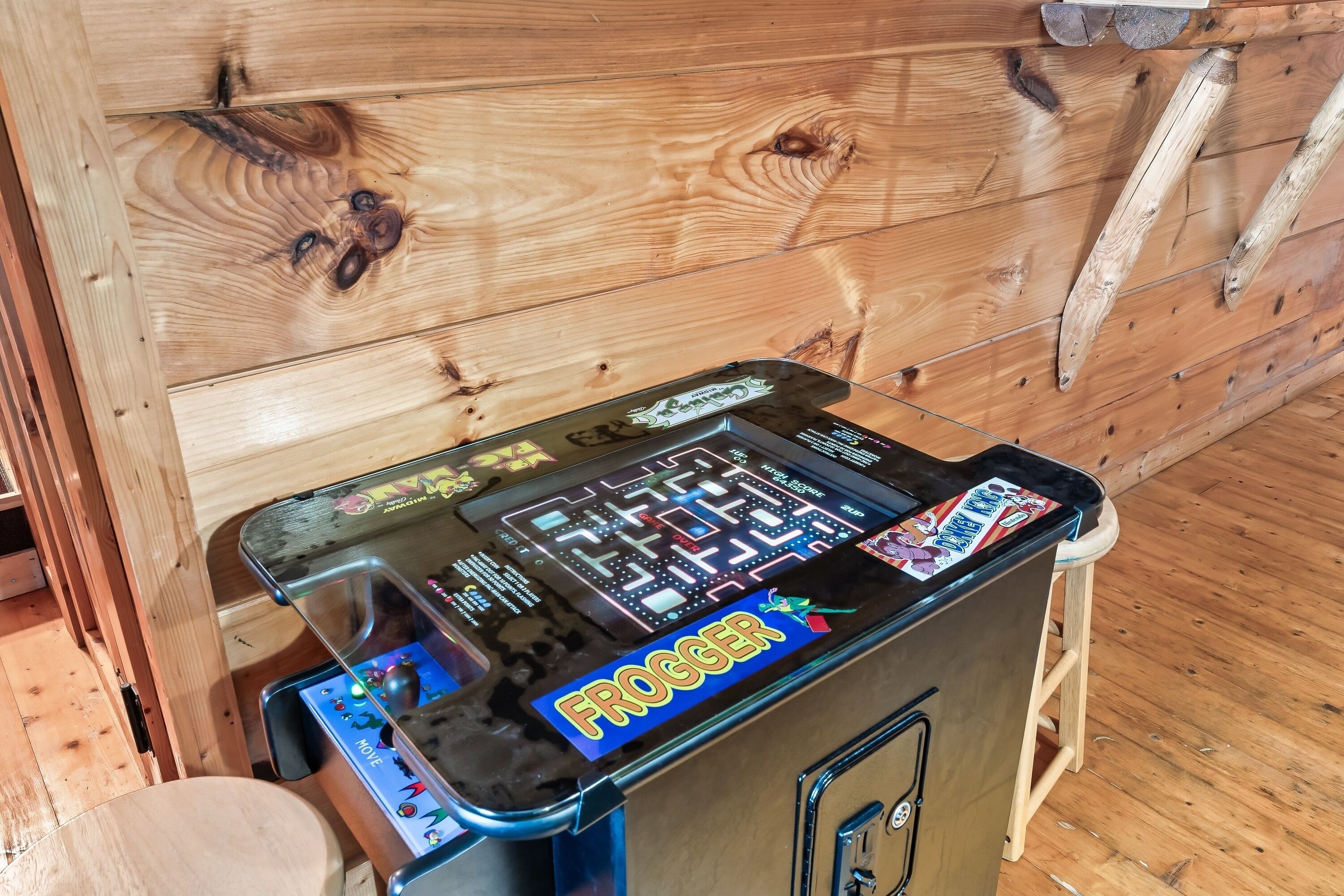 A claw machine arcade game with the word "FROGGER" on the front, placed against a wooden wall.