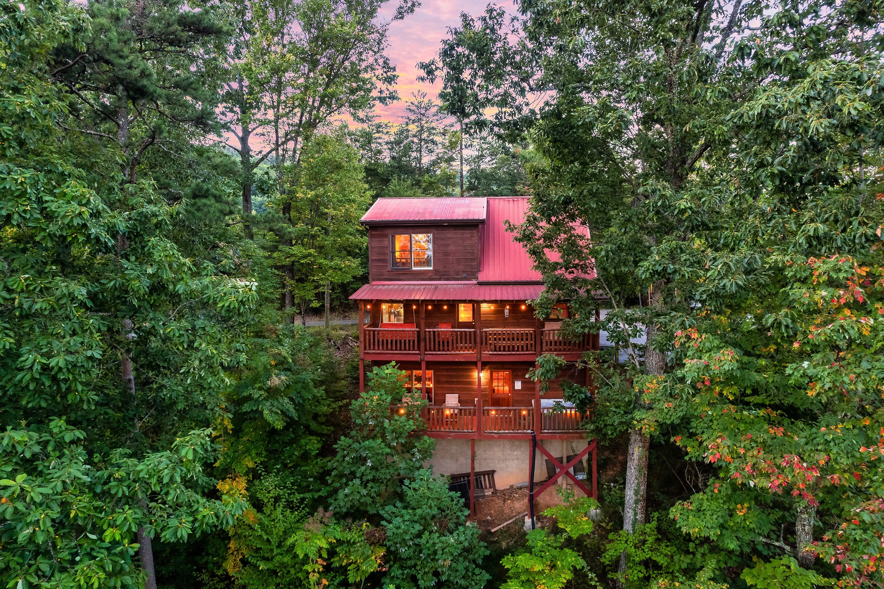 A multi-story wooden cabin with a red roof, surrounded by dense forest.