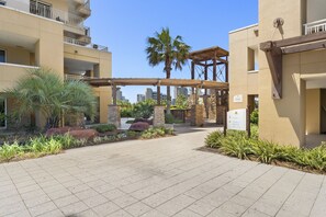 A hotel entrance with a paved walkway, palm trees, and a sign indicating the direction to Tower 1, Tower 2, Pool, and Tiki Hut.