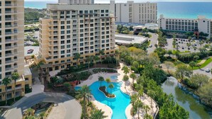 Un resort con varios edificios altos, una piscina central y una zona ajardinada con palmeras.