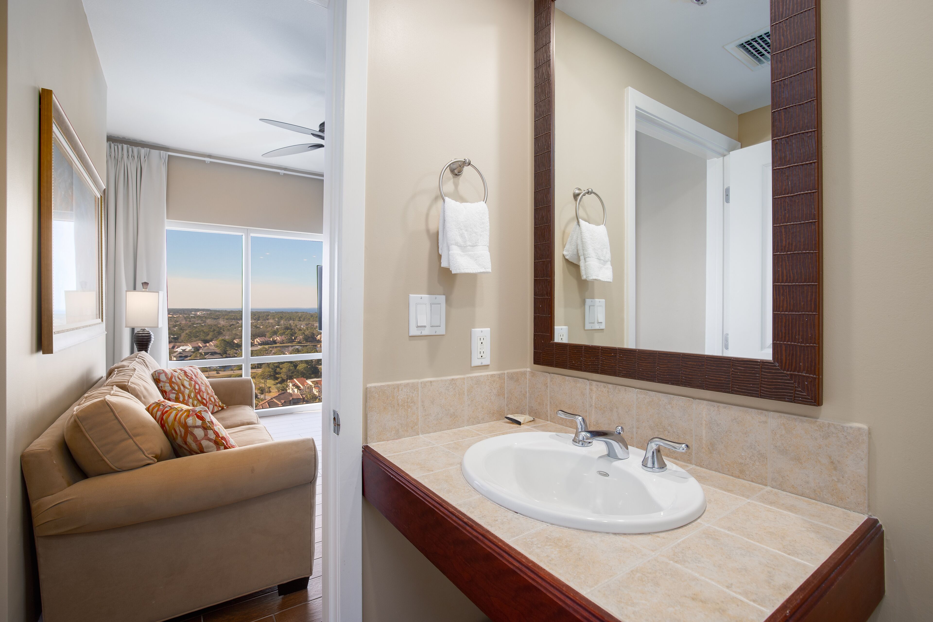 A bathroom with a large window, a sofa with cushions, a sink, and a mirror.