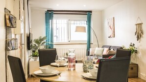 Comedor con una mesa redonda para cuatro personas, un sofá al fondo y una ventana con cortinas.