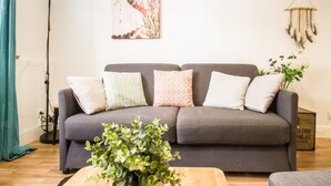 Un sofá gris con cojines estampados, una mesa de centro de madera con plantas verdes, y una obra de arte colgada en la pared.