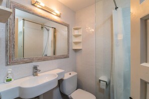 Et badeværelse med hvid vask, spejl og toilet.