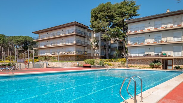 En swimmingpool med en röd kant, belägen intill en hög byggnad med flera våningar, balkonger och en fasad av sten.