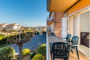 En balkon med et bord og stole, udsigt til gaden, og en bygning med altaner.
