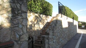 A stone staircase leading up to a gated entrance, surrounded by a stone wall and greenery.