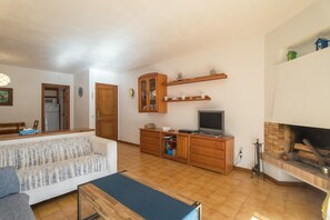 A living room with a sofa, TV, wooden cabinet, fireplace, and a kitchen area in the background.
