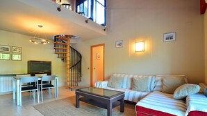 A spacious living area with a sofa, coffee table, and dining set. A spiral staircase leads to an upper level.