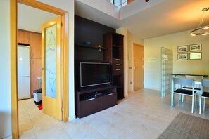 Uma sala de estar moderna com uma grande televisão de tela plana, prateleiras embutidas e um espaço de jantar com mesa e cadeiras de vidro.