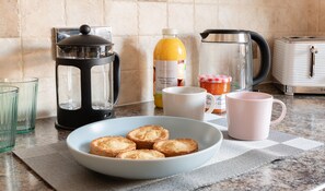 A kitchen counter with a coffee press, a bottle of orange juice, a jar of marmalade, a toaster, and a bowl of toast.