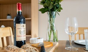 A bottle of wine, a glass, cheese, and bread on a wooden table.