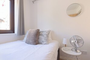 Ein Schlafzimmer mit einem Bett, Kissen, einem runden Spiegel und einem Standventilator.