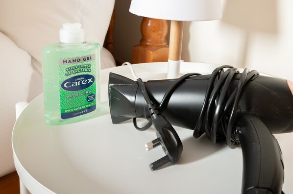 A hand sanitizer bottle and a black hair dryer on a white table.