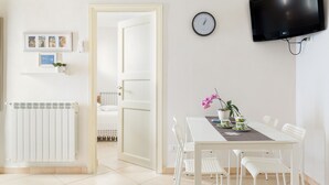 Una habitación moderna y luminosa con una mesa de comedor blanca, sillas, un televisor de pantalla plana y un reloj en la pared.