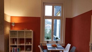 A dining area with a table and chairs, a bookshelf, and a window with a view of houses. - Vacation apartment "Villa am Kurpark" - Maisonette (Friedrichroda)