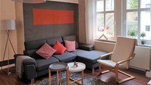 A modern living room with a grey sectional sofa, red and white patterned cushions, a round coffee table, and a wooden chair. - Vacation apartment "Villa am Kurpark" - Maisonette (Friedrichroda)