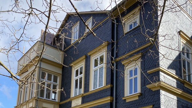 A multi-story building with a dark exterior and yellow trim, featuring multiple windows and a visible chimney. - Vacation apartment "Villa am Kurpark" - Maisonette (Friedrichroda)