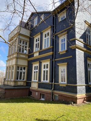 A multi-story building with a dark exterior and yellow trim, featuring multiple windows and a visible chimney.