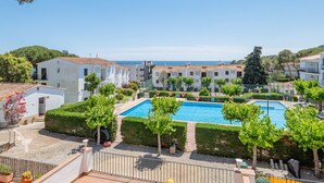 A pool area with a clear view of the sea, surrounded by neatly trimmed hedges and small trees.