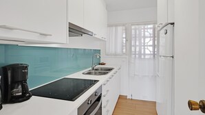 A modern kitchen with white cabinets, a black countertop, a coffee maker, and a window with sheer curtains.