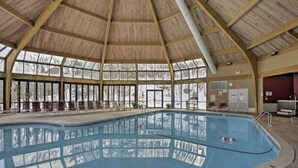 An indoor swimming pool with a high wooden ceiling and large windows.