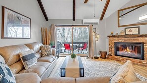 A cozy living room with a leather sofa, a fireplace, and a large window overlooking a deck.