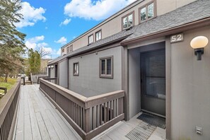 A modern two-story building with a grey exterior, a wooden deck, and a garage door.