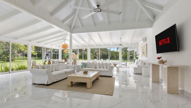 A spacious living room with white furniture, a large TV mounted on the wall, and a view of the outdoors. - Close to Minitas Beach (La Romana)