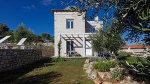 Una casa in pietra con un balcone, immersa nel verde sotto un cielo azzurro intenso.